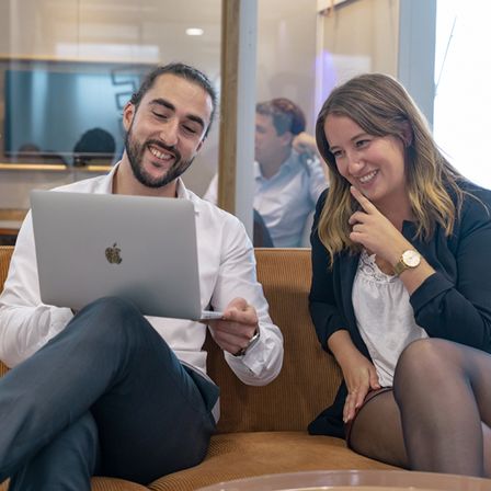 Two smiling employees looking at a laptop.
