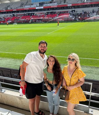 Three people in front of the lawn at the Stade Auguste Delaune in Reims during an OL match.